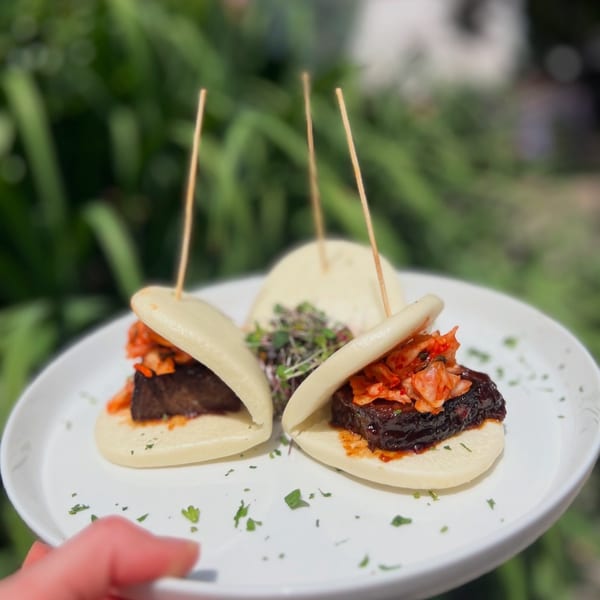 Three New American bao buns with braised short rib and kimchi on a white plate.