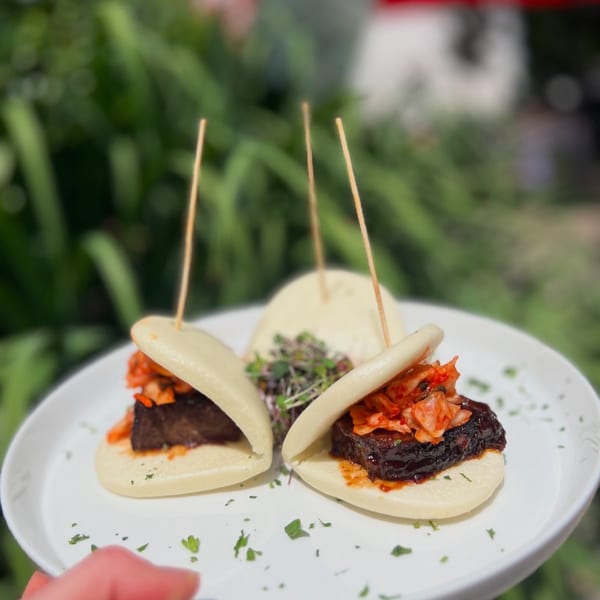Three bao buns with dark meat and kimchi, garnished with microgreens, on a white plate.