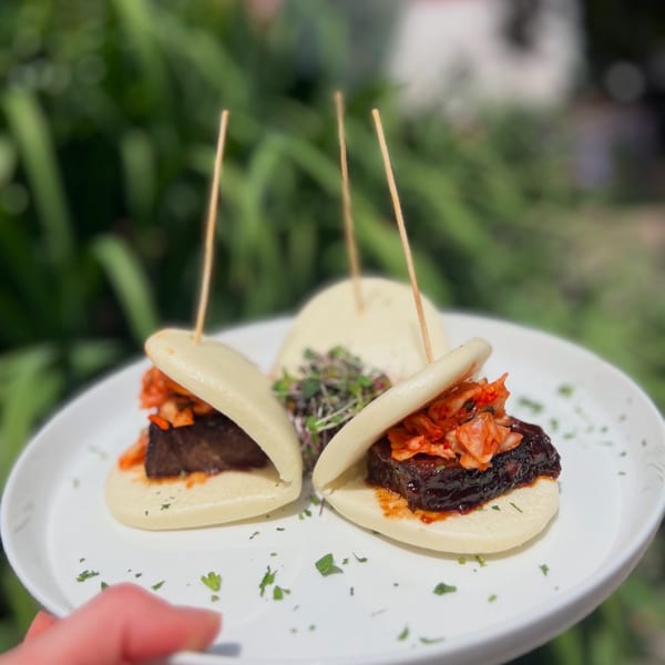 Three bao buns with dark meat and kimchi, garnished with microgreens on a white plate.