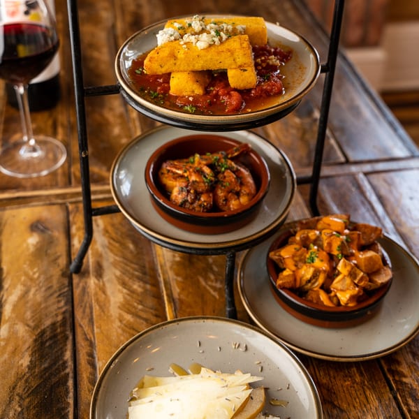 A tiered stand holds New American dishes: polenta, shrimp, potatoes, and cheese with pears.