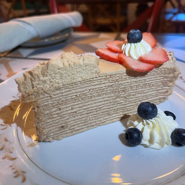 A slice of layered crepe cake with whipped cream, strawberries, and blueberries on a white plate.