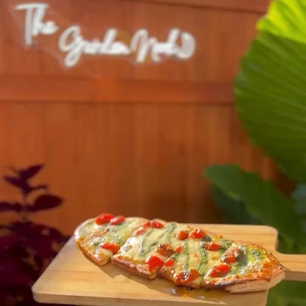 Rectangular vegetable-topped pizza slices arranged on a wooden serving board in a warmly lit restaurant setting.