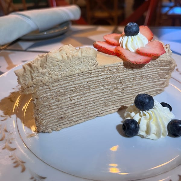 A slice of Under the Moon's crepe cake with strawberries, blueberries, and whipped cream on a white plate.