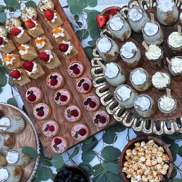 An overhead view of a dessert spread featuring mini tarts, parfaits, and pastries with fruit.