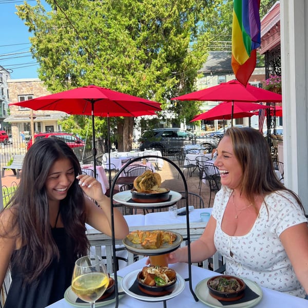 Two women laughing at an outdoor table with a tiered platter of New American dishes.