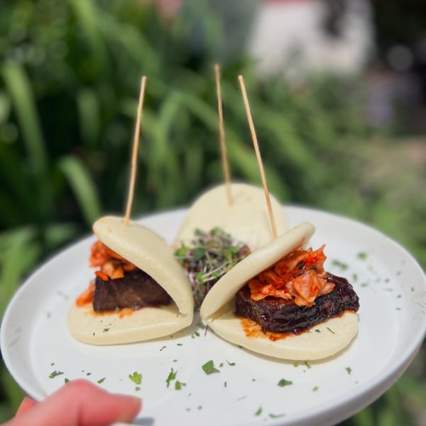 Three Under the Moon pork belly bao buns with kimchi and microgreens on a white plate.