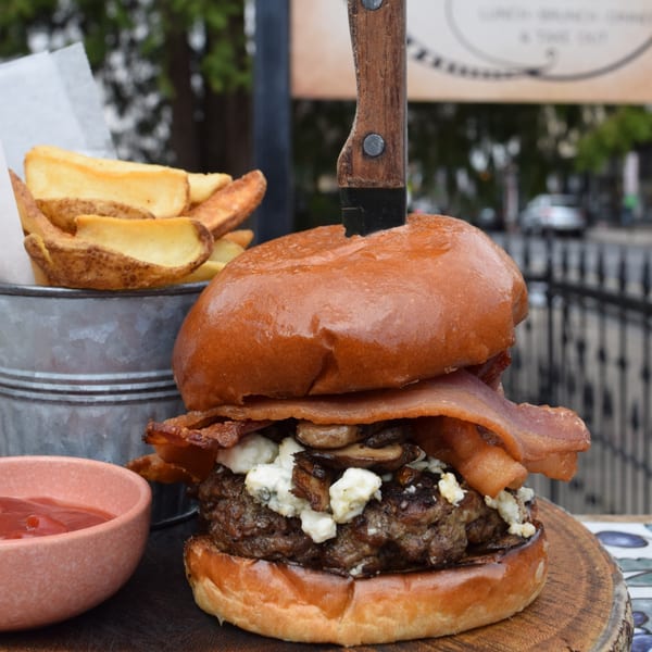 A bacon, mushroom, and blue cheese burger with a knife, served with potato wedges and ketchup.