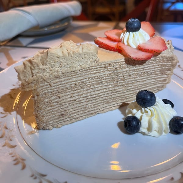 A slice of layered crepe cake with strawberries, blueberries, and whipped cream on a white plate.